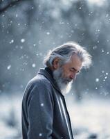 Elderly man with gray beard looks pensively while snow falls softly around him in a winter landscape. photo