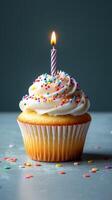 Delicious birthday cupcake with frosting and a single lit candle surrounded by colorful sprinkles photo