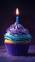 Colorful cupcake with a lit candle and vibrant frosting on a purple background for a birthday celebration photo