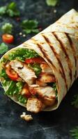 Grilled chicken wrap filled with fresh vegetables and herbs on a dark background photo