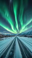 Colorful auroras illuminate a snow-covered road in a remote mountain landscape at night photo