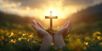 Hands holding a cross surrounded by flowers with a sunset in the background at a serene outdoor location photo