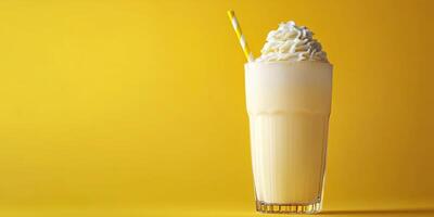 Frosty creamy beverage served in a glass with whipped topping and a straw against a bright yellow background photo