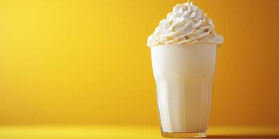 Creamy milkshake topped with whipped cream in a clear glass against a bright yellow background photo