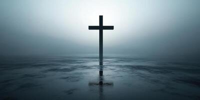 Dark silhouette of a cross reflecting in still water during foggy dawn near a tranquil landscape photo