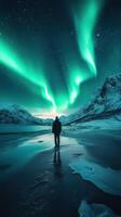 Bright auroras dance over snowy mountains while a lone figure stands in awe at night in a remote location photo
