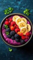 Colorful fruit smoothie bowl topped with berries and bananas on a dark surface photo