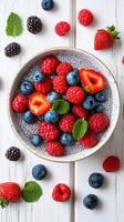Fresh berries arranged beautifully in a bowl on a wooden table with mint leaves on a sunny day photo