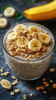 Healthy breakfast bowl with banana slices and granola on top, featuring chia seeds and oats in a glass photo