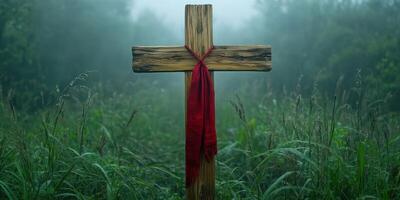 Rustic wooden cross adorned with a red ribbon is surrounded by misty grass in a serene and quiet landscape photo