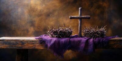 Symbolic arrangement of crown of thorns and cross on rustic table with purple cloth in an atmospheric setting photo