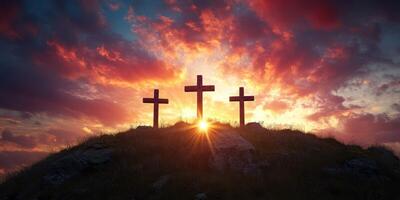 Three crosses stand silhouetted against a dramatic sunset sky over a hillside photo