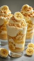 Delicious banana dessert with layers of cream, banana slices, and crumbs served in clear glass cups photo