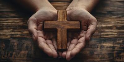 Hands holding a wooden cross against a rustic wooden background, symbolizing faith and devotion photo