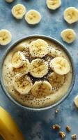 Healthy banana smoothie bowl topped with chia seeds and sliced bananas served in a blue bowl on a light background photo