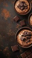 Rich chocolate mousse served in dark bowls with chocolate squares on a textured surface photo