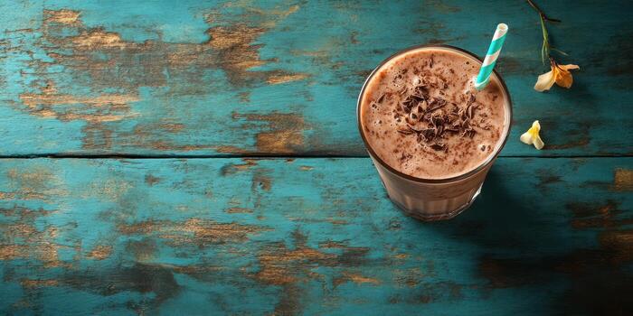 Creamy chocolate drink served in a clear glass on a rustic turquoise table with a striped straw photo