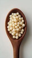 Delicate white tapioca pearls displayed in a wooden spoon on a neutral background for culinary use photo