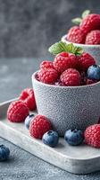 Fresh raspberries and blueberries arranged in a textured bowl with mint leaves on a rustic table photo