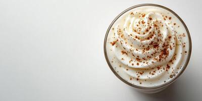 Warm beverage topped with creamy whipped cream and cinnamon sprinkles served in a clear glass on a light background photo