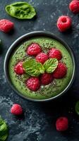 Delicious green smoothie bowl topped with fresh raspberries and mint on a dark textured background photo