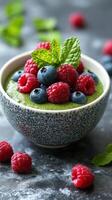 Fresh green smoothie bowl topped with blueberries, raspberries, and mint leaves displayed on a textured background photo