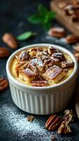 Delicious pecan dessert in a white ramekin topped with powdered sugar and fresh pecans on a dark kitchen countertop photo