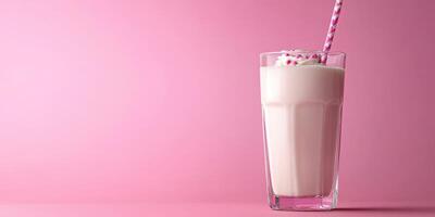 Delicious milkshake in a tall glass with whipped cream and a straw against a pastel pink background photo