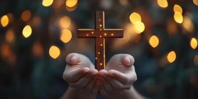 Hands holding a wooden cross illuminated by warm lights in a serene atmosphere during evening hours photo