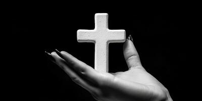 Hand holding a white cross against a dark background creating a striking contrast of faith and spirituality photo