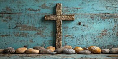 Wooden cross placed on a blue wooden background with smooth pebbles arranged below it photo