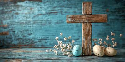 Rustic wooden cross with decorated eggs and dried flowers on a weathered blue background photo