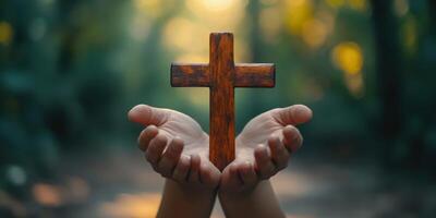 Hands holding a wooden cross in a serene forest setting during golden hour light photo