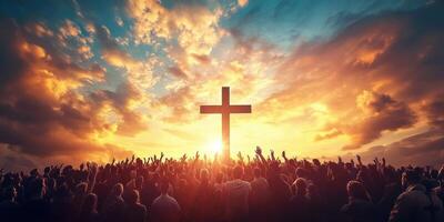 Crowd of worshippers gather at sunset around a large cross under a colorful sky photo