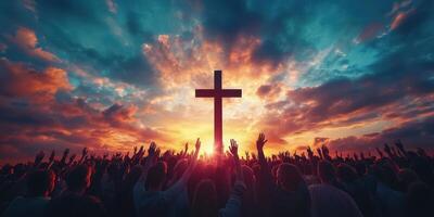 Crowd worshipping at sunset with raised hands in front of a large cross in a peaceful outdoor setting photo