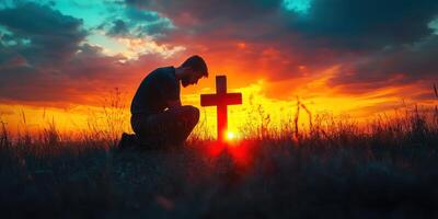 Person kneeling by a wooden cross at sunset in an open field during a moment of reflection photo