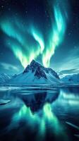 Vibrant northern lights illuminate the snow-capped mountain and calm waters at night in a breathtaking landscape photo