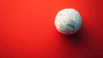 A white ball of yarn rests on a red background surface photo