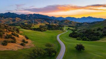 Scenic Winding Road Through Lush Green Valley at Sunset with Wind Turbines and Mountains photo