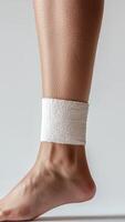 Close-up of a foot with a bandage wrapped around the ankle on a neutral background photo