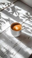 Cup of coffee resting on a wooden table with shadows from leaves photo