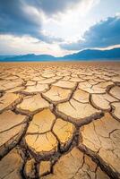 Cracked dry earth landscape under blue sky with mountains in the distance photo