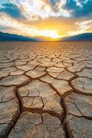 Cracked dry earth landscape during sunset with a colorful sky and distant mountains photo