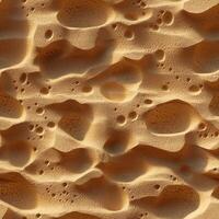 Textured sand surface with undulating patterns and small pits photo
