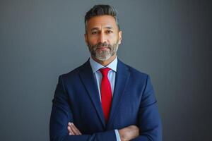Confident South Asian man in a suit poses with arms crossed, exuding professionalism against a neutral background. photo
