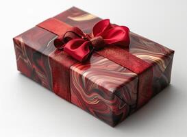 A beautifully wrapped gift box in red and gold tones, featuring a glossy ribbon and a decorative bow. photo