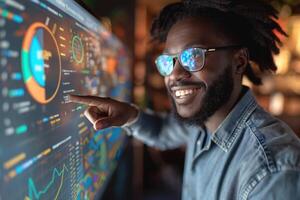A Black male analyst with glasses engaging with a digital dashboard, smiling as he points to data visualizations. photo