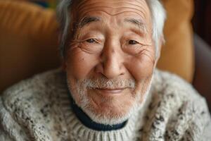 Elderly Asian man with a warm smile, wearing a cozy sweater, radiating joy and wisdom in a comfortable indoor setting. photo