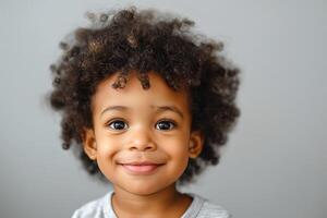 A joyful Black boy with curly hair smiles brightly against a neutral backdrop. photo
