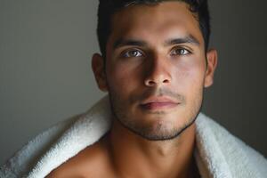 Close-up portrait of a young Hispanic man with piercing eyes, wrapped in a white towel, showcasing a calm and introspective mood. photo